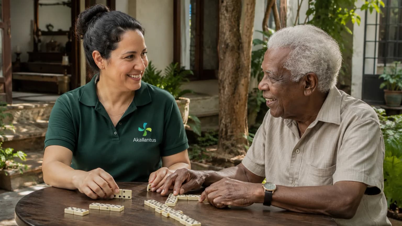Cuidadora da Akallantus joga dominó com um senhor idoso em uma varanda ajardinada em Santo Amaro, São Paulo.